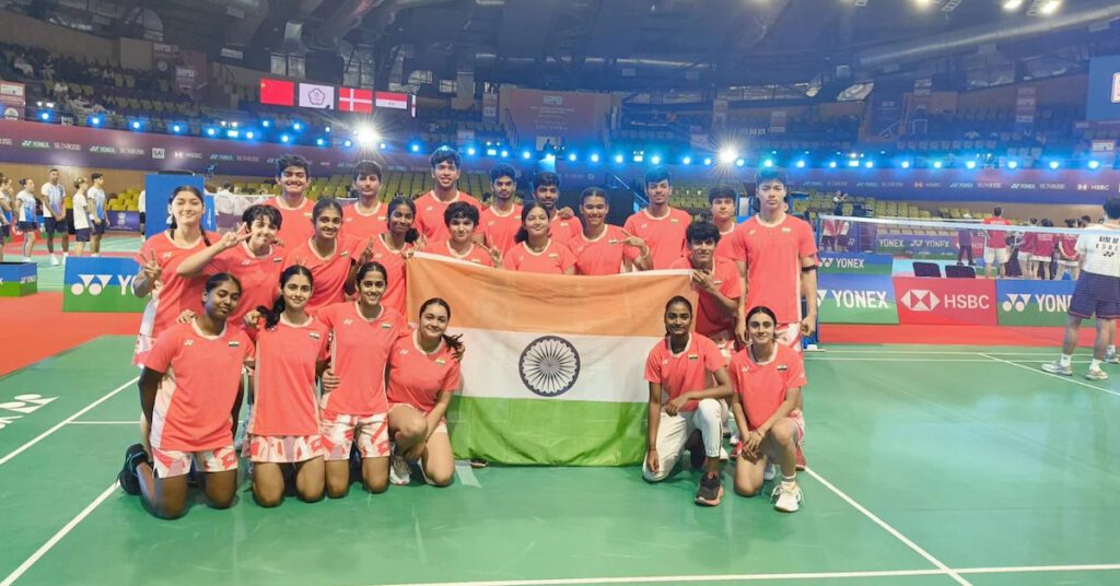 Indian badminton team posing with national flag at indoor stadium